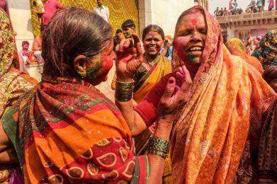 Two women smiling amidst a crowd of people at the Holi color festival